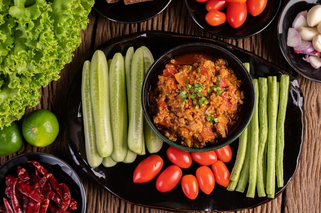 Сладкая свинина в черной миске с огурцами, длинной фасолью, помидорами и гарнирами