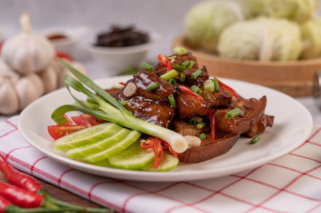 Sweet pork on a white plate with chopped scallions, chili, lime, cucumber, tomato, and garlic.