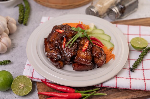 Sweet pork on a white plate with chopped scallions, chili, lime, cucumber, tomato, and garlic.