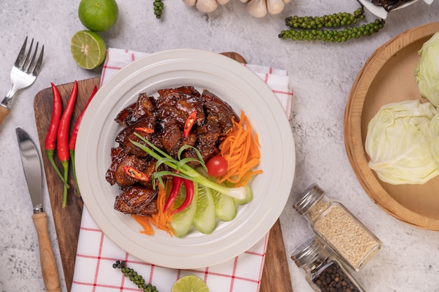 Free photo sweet pork on a white plate with chopped scallions, chili, lime, cucumber, tomato, and garlic.