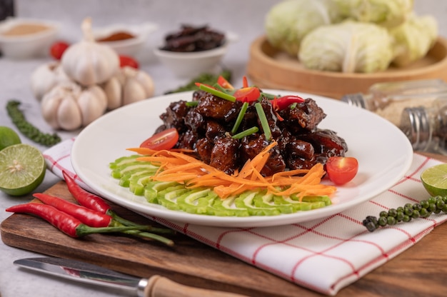 Sweet pork in a white plate with chopped scallions, chili, lime, gourd, tomato and garlic.