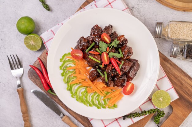 Sweet pork in a white plate with chopped scallions, chili, lime, gourd, tomato and garlic.