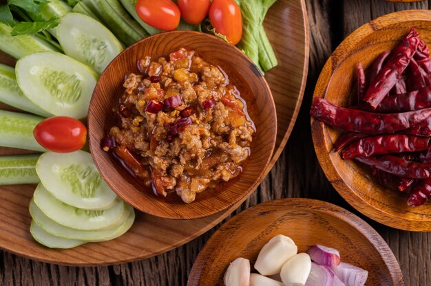 Sweet pork in a wooden bowl with cucumber, long beans, tomatoes, and side dishes.