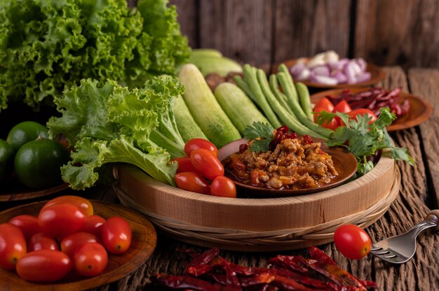 Sweet pork in a wooden bowl with cucumber, long beans, tomatoes, and side dishes.