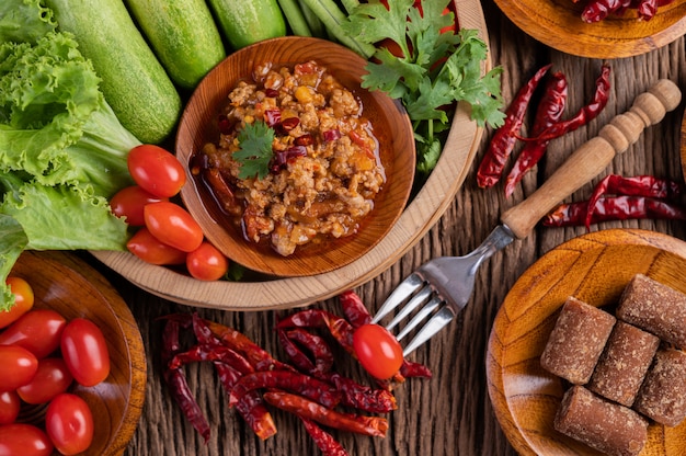 Free photo sweet pork in a wooden bowl with cucumber, long beans, tomatoes, and side dishes.