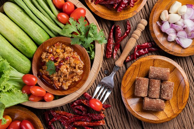 Sweet pork in a wooden bowl with cucumber, long beans, tomatoes, and side dishes.