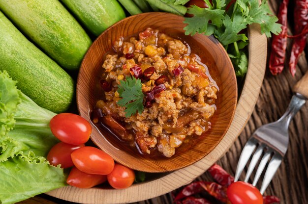 Sweet pork in a wooden bowl with cucumber, long beans, tomatoes, and side dishes.