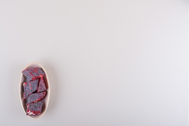Сладкие красные конфеты с орехами в бежевой миске на белом фоне. Фото высокого качества
