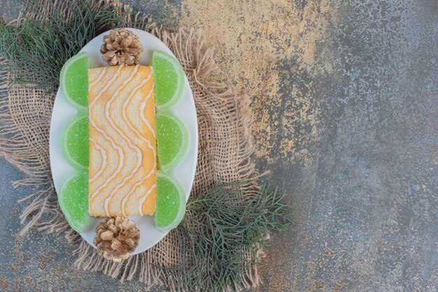 Sweet roll with green marmalades and pinecones on a white plate. High quality photo