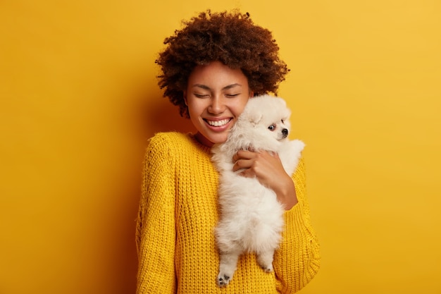 陽気なアフロの女性の甘いショットは彼女のスピッツ犬を大きな愛で抱きしめます