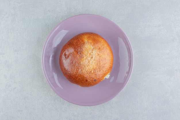 Sweet single bun on purple plate. 