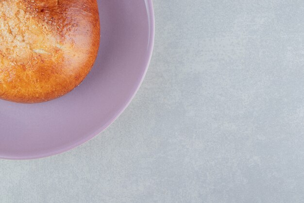 Sweet single bun on purple plate. 