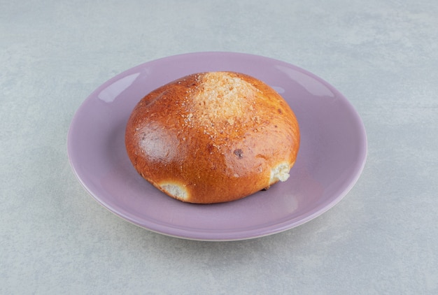 Sweet single bun on purple plate. 