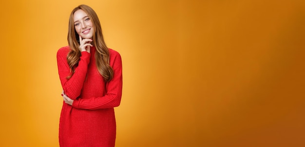 Free photo sweet and tender redhead woman with cute freckles in red knitted dress tilting head touching face wi