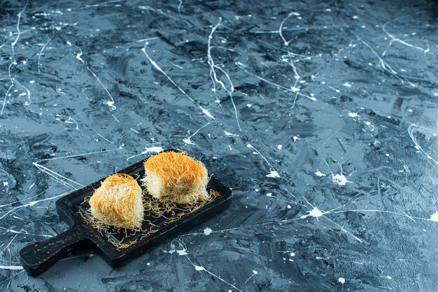 Sweet Turkish dessert kadayif on a board, on the blue table. 