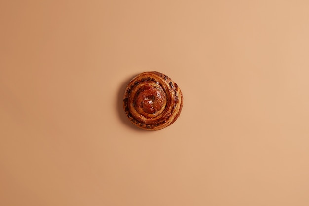 Sweet yummy freshly baked swirling cinnamon bun for your snack or breakfast. Appetizing unhealthy puff cake on beige background. Confectionery and bakery concept. Whole delicious french roll