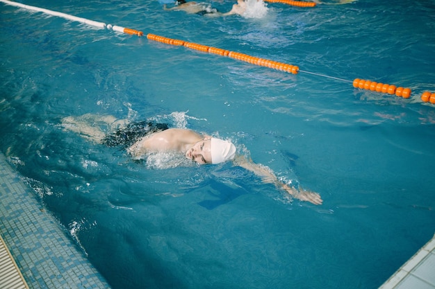 Пловец в кепке тренируется в бассейне. Вид сверху со стороны бассейна.