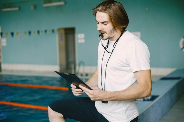 Swimming coach standing by the pool. Checking swimming records. Holding clipboard.