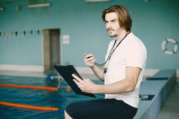 Swimming coach standing by the pool. Checking swimming records. Holding clipboard.