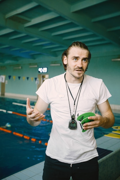 Swimming equipments for sportsmen. Male coach standing by pool and guide how to use swimming hand paddles.