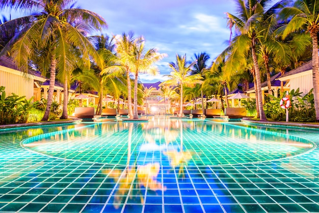 Swimming pool with palm trees in resort hotel at night