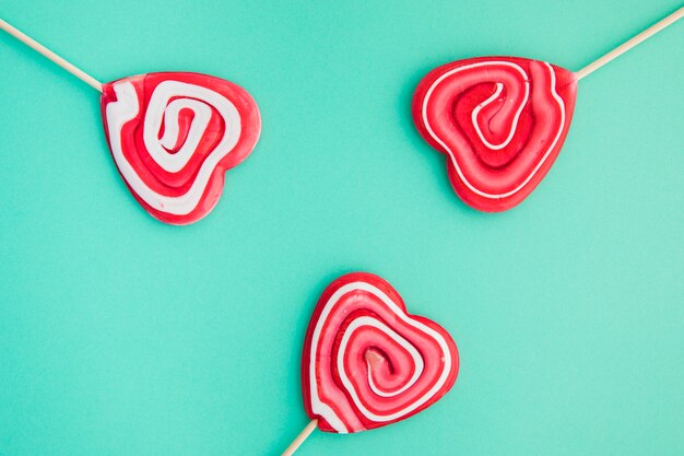 Swirl heart shape red lollipops on green background