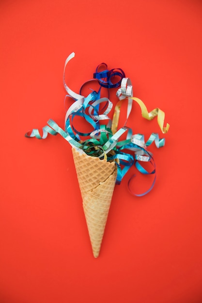 Swirled colorful streamers inside the waffle cone on red background