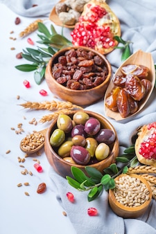 Symbols of judaic holiday tu bishvat, rosh hashana new year of the trees. mix of dried fruits, date, fig, grape, barley, wheat, olive, pomegranate on a marble table.