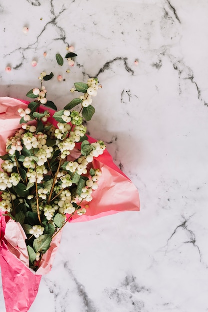 Symphoricarpos albus; common snowberry twigs wrapped in pink paper on marble backdrop