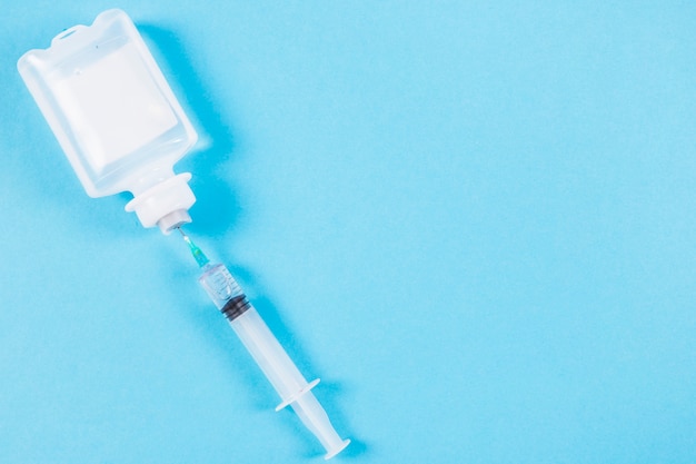 Free photo syringe inserted in normal saline solution plastic bottle on blue background