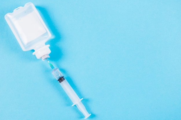 Syringe inserted in normal saline solution plastic bottle on blue background