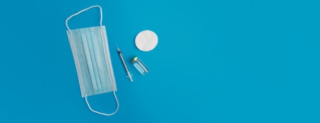 Шприц медицинская маска и ампула с лекарством на синем фоне панорамы Premium Фотографии