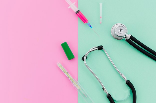 Syringe; stethoscope; thermometer on pink and mint green background