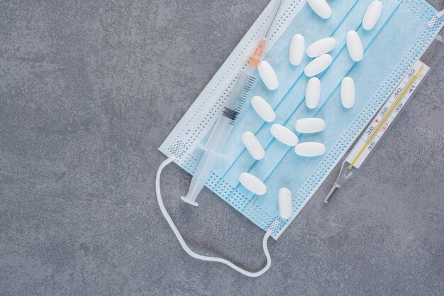 Syringe, thermometer and pills on medical mask.