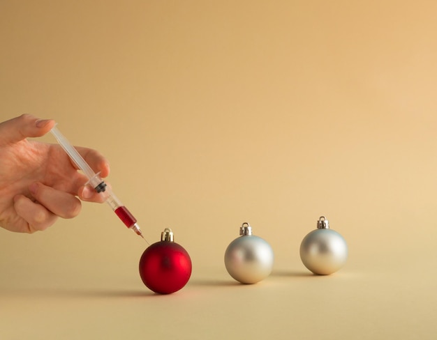 Syringe and vaccination with human hand and christmas baubles minimal new year or pandemic idea