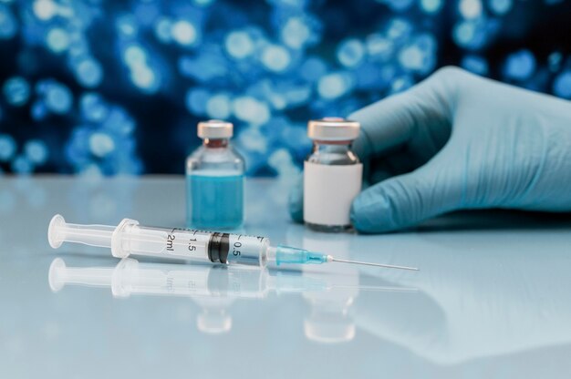 Syringe and vaccine bottle on the table with hand in glove