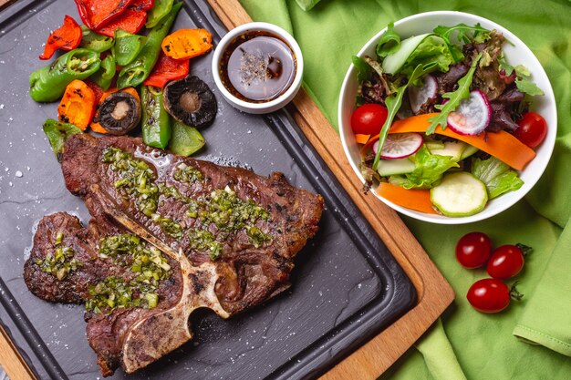 T-bone steak with greens bell pepper tomato carrot mushroom with green salad in bowl top view