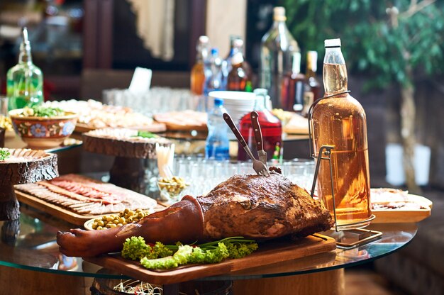 Стол полный еды и алкогольных напитков в ресторане. Копченая свинина подается на деревянной тарелке.