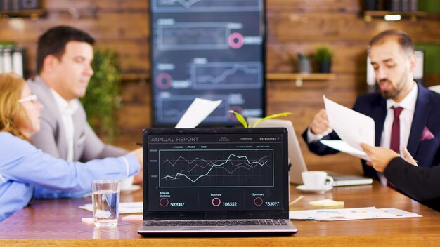 On the table laptop showing charts in the conference room. Business people having an important discussion.