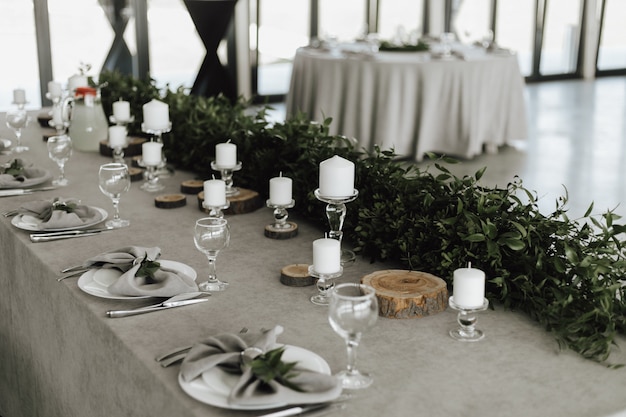 Free photo table serving, decoration with greenery and white candles on grey table