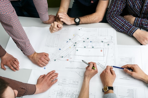 Free photo table with blueprints and hands holding pencils