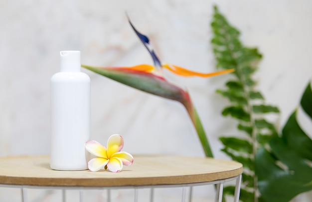 Free photo table with clear white bottle and green palm leaves over marble wall