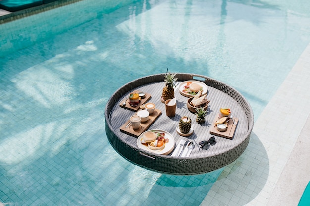 Table with cups of cappuccino and plates of fruits. exotic lunch in swimming pool.