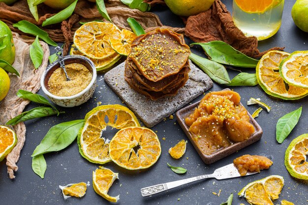 Table with dry citruses and raw pancakes near a bowl full of tangerine jam