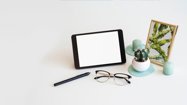 Table with tablet near photo frame, cactus, pen and eyeglasses