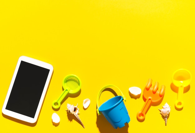 Tablet and beach toys on colorful surface