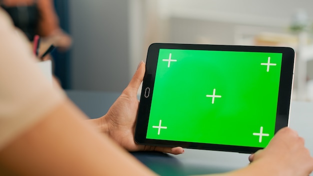 Tablet computer with mock up green screen chroma key display standing on table desk. Freelancer woman browsing on isolated device for online web communication in home office room