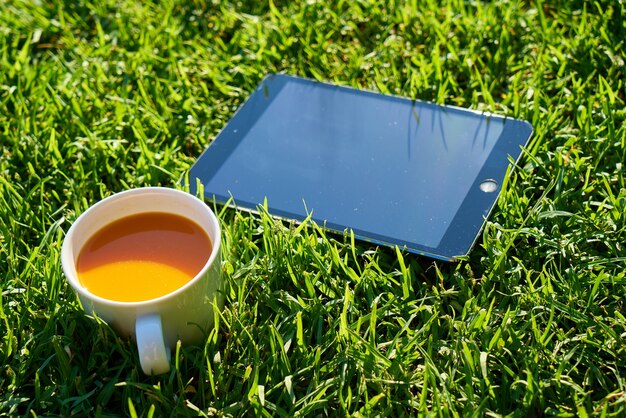緑の芝生の上でタブレットとコーヒーカップ