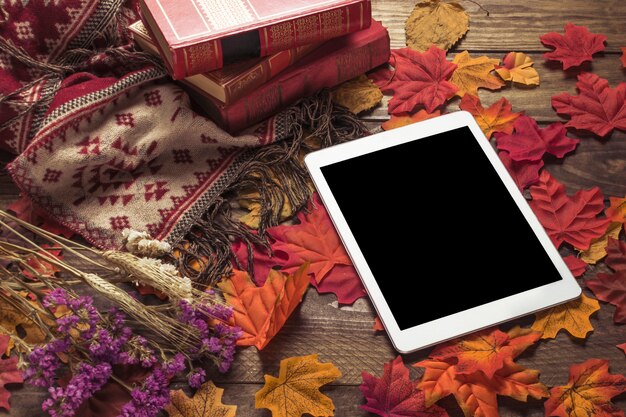 Tablet on leaves near books and flowers