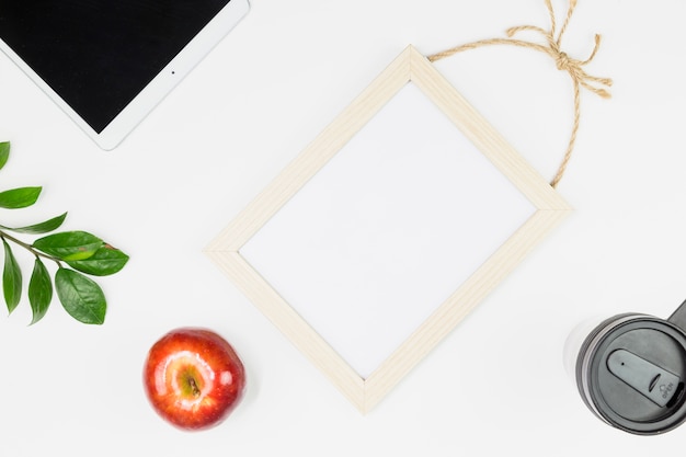 Tablet near apple, plant twig, cup and photo frame